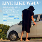 Surfer op blote voeten in de oversized zwarte poncho bij zijn auto, helemaal in de Live Like WOLV sfeer