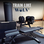 Zwarte WOLV yogamat rechtop gerold in een home gym naast verstelbare dumbbells en een halterbank