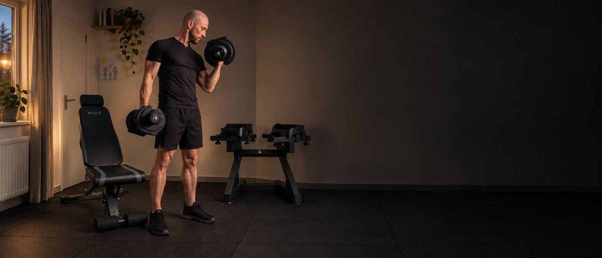 Man training with WOLV adjustable dumbbells in a living room home gym at dusk