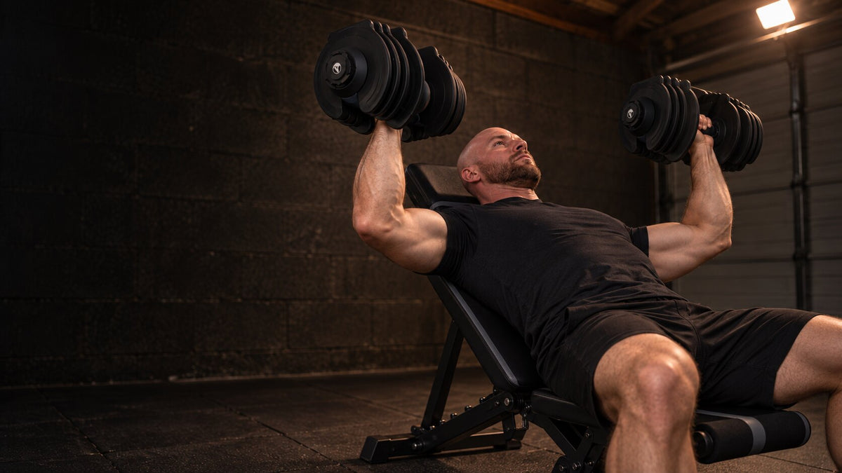 Man doing an incline dumbbell press on a WOLV adjustable bench in a dark home gym