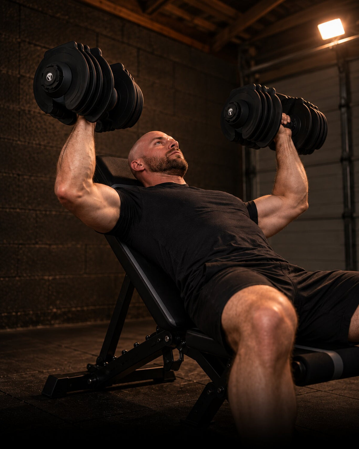 Man doing an incline dumbbell press on a WOLV adjustable bench in a dark home gym, portrait crop for phones