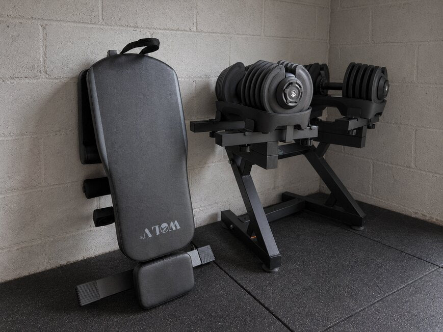 Folded WOLV adjustable bench next to a WOLV dumbbell stand with two adjustable dumbbells