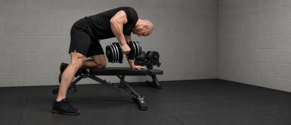 Man doing a one-arm dumbbell row on a WOLV bench in a home gym